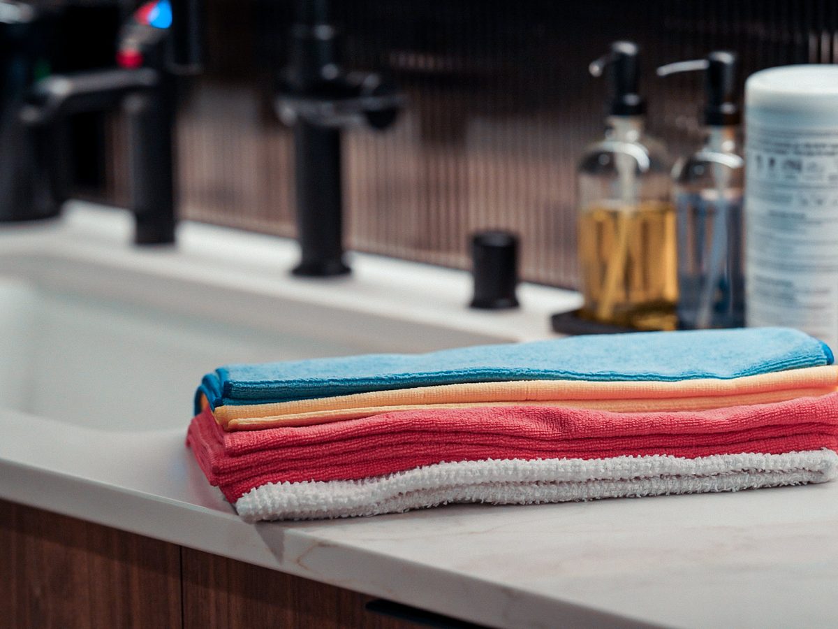 Stack of blue, yellow, red and white microfiber cloths on a restroom counter, with soap dispensers behind.