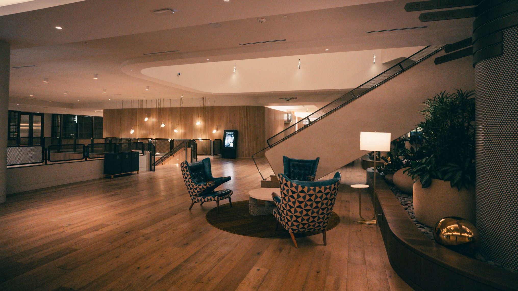 Empty office building lobby at night with wood floors, lounge chairs, planters and a staircase.