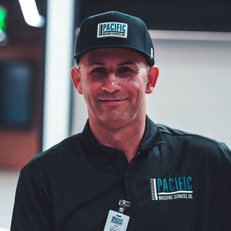 Smiling PBS crew member in a black PBS cap, polo and ID badge.