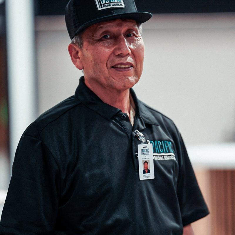 Smiling PBS crew member in a black PBS cap and polo with ID badge.