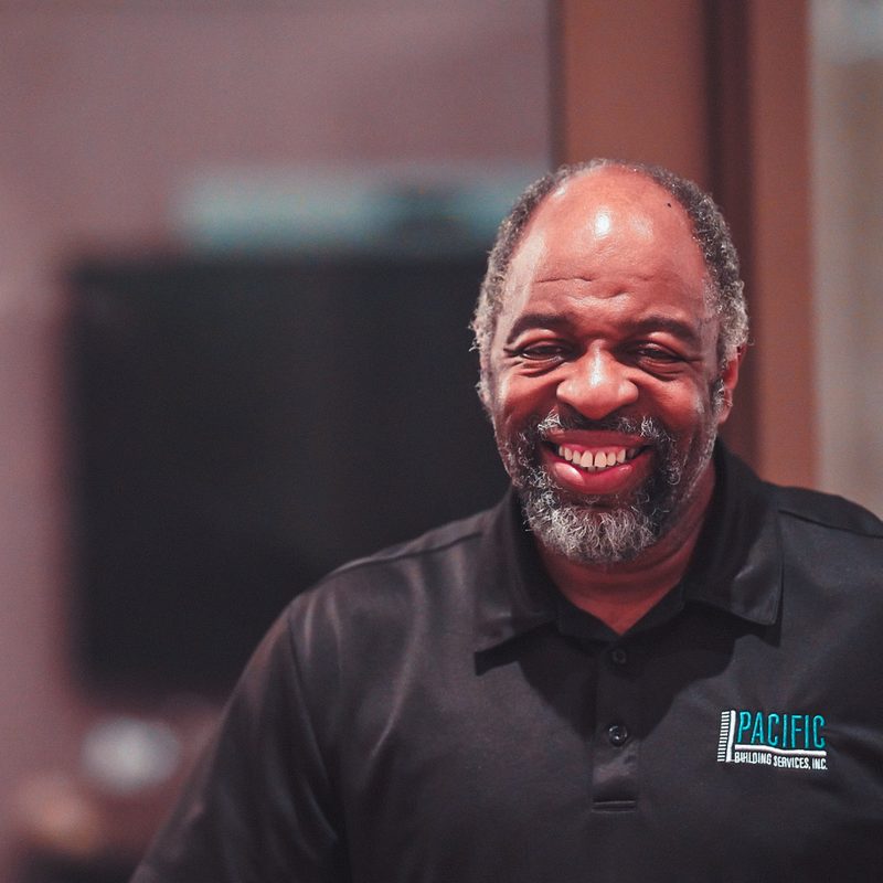 Smiling PBS team member with a gray beard, wearing a black PBS polo.