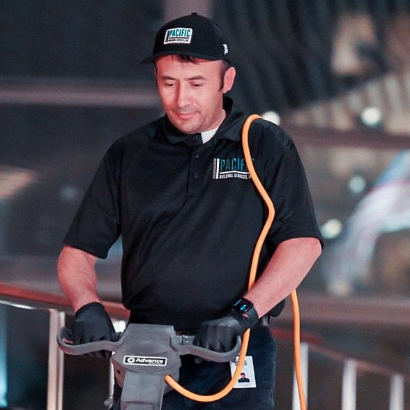 PBS floor technician in a black cap and polo running a floor burnisher.